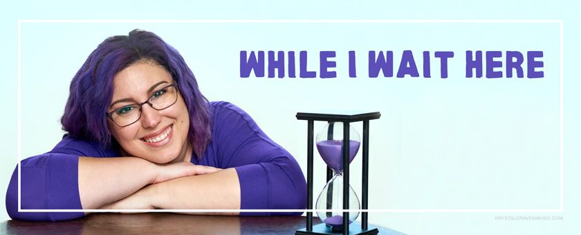 Krystal Craven wearing a purple shirt and glasses, smiling while laying her head on her arms which are folded on a wooden table. There is an hourglass to the right side of her with purple sand in it. The title "While I Wait Here" is printed above the hourglass.