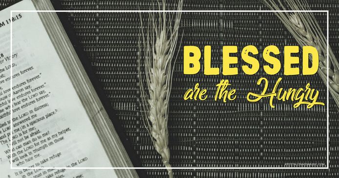 The devotional title text "Blessed are the Hungry" overlaying a top down image of an open Bible on a placemat with a couple strands of wheat laying next to it.