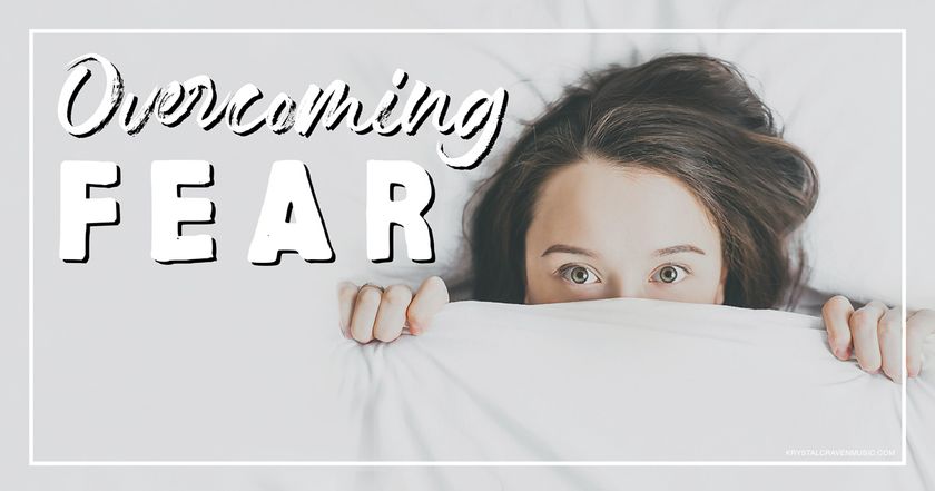 The devotional title text of "Overcoming Fear" overlaying a woman laying in bed holding the top sheet over part of her face so that only her eyes up are seen, and she has a scared look in her eyes.
