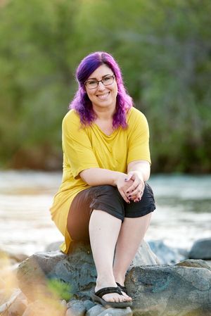 Krystal smiling while sitting on rocks with a stream in the background